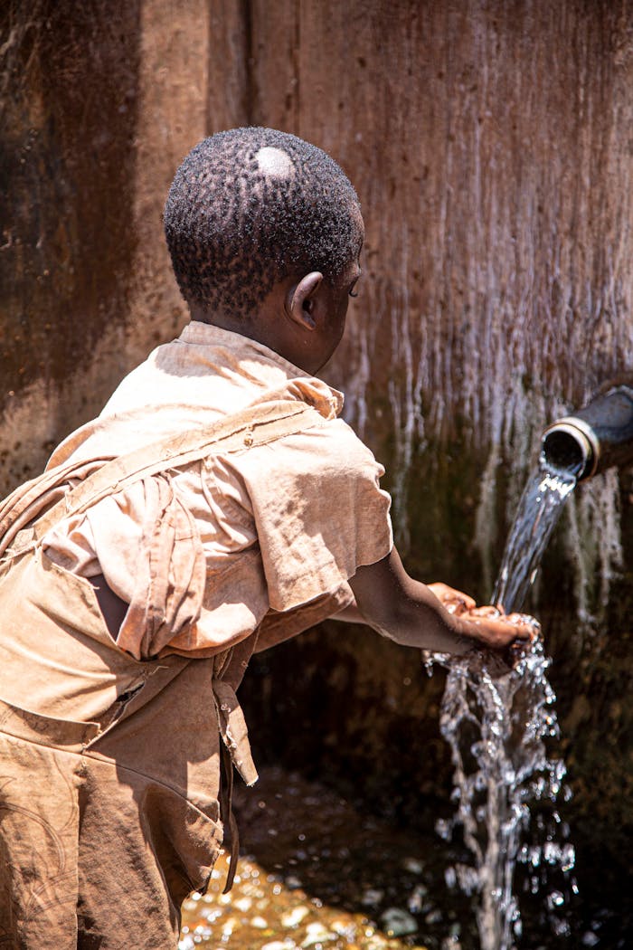 A child gathers clean water from an outdoor tap, highlighting access to essential resources.